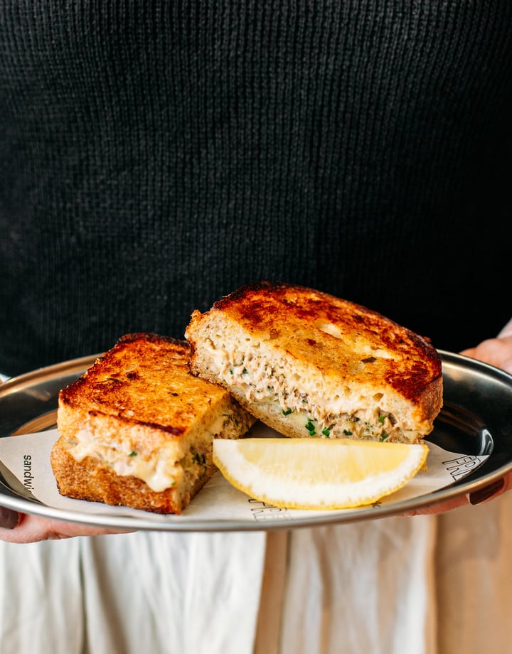 A person holding a plate of grilled cheese and tuna toasted sandwich.