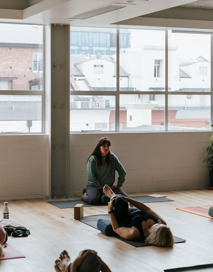 A yoga teacher taking a class of students lying on their backs.