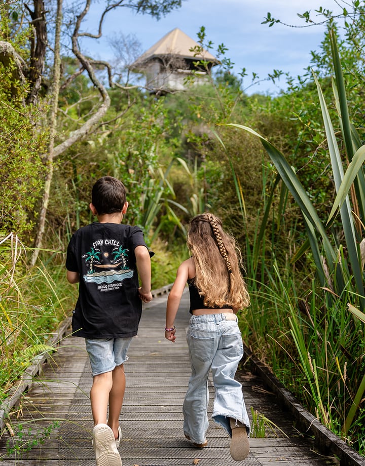 Two children running on the boardwalk in and amongst native bush.
