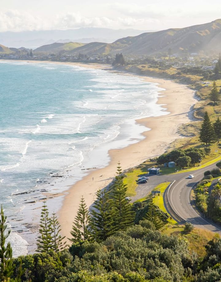 Road runs alongside the coastline, the waves on the beach meet the sand.