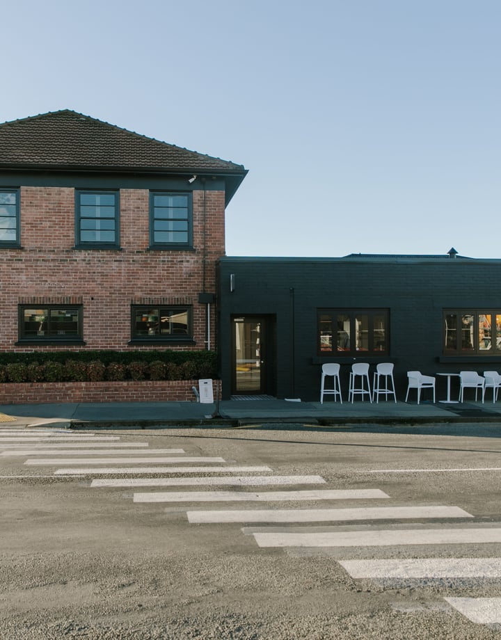 A view of a black and brick building from across the street on a sunny day.