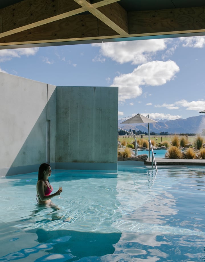 A woman walking through the water at Opuke Thermal pools with the Southern Alps in the background.