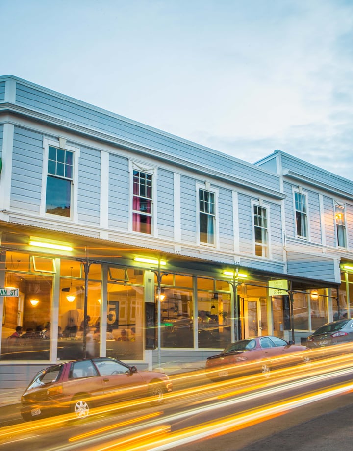 A photo of a blue building with cars whizzing by out front at dusk.