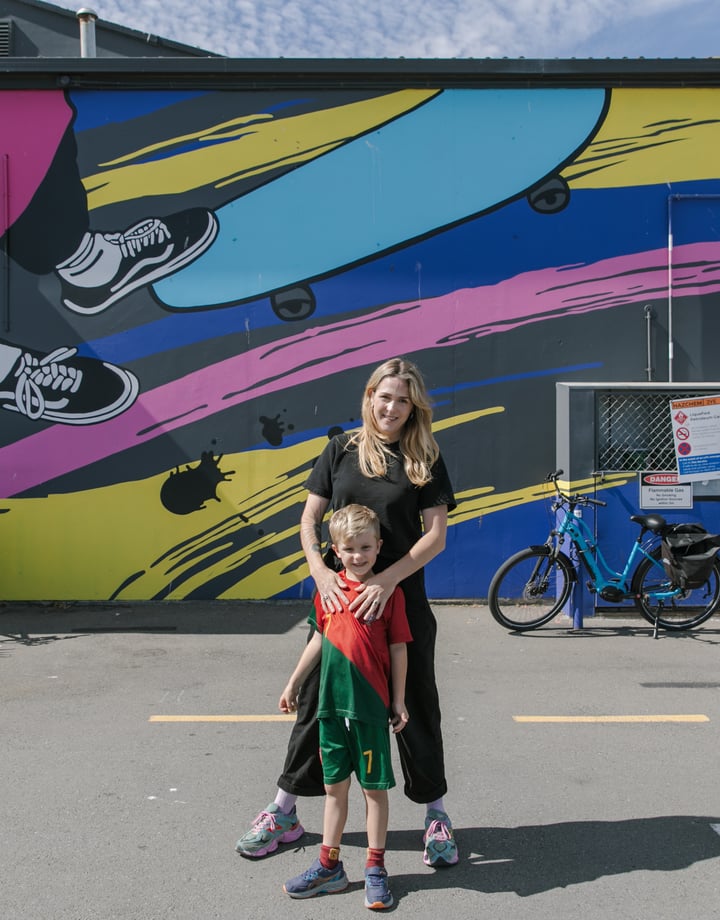 A woman and her son standing in front of a colourful mural painted on the exterior of a building.