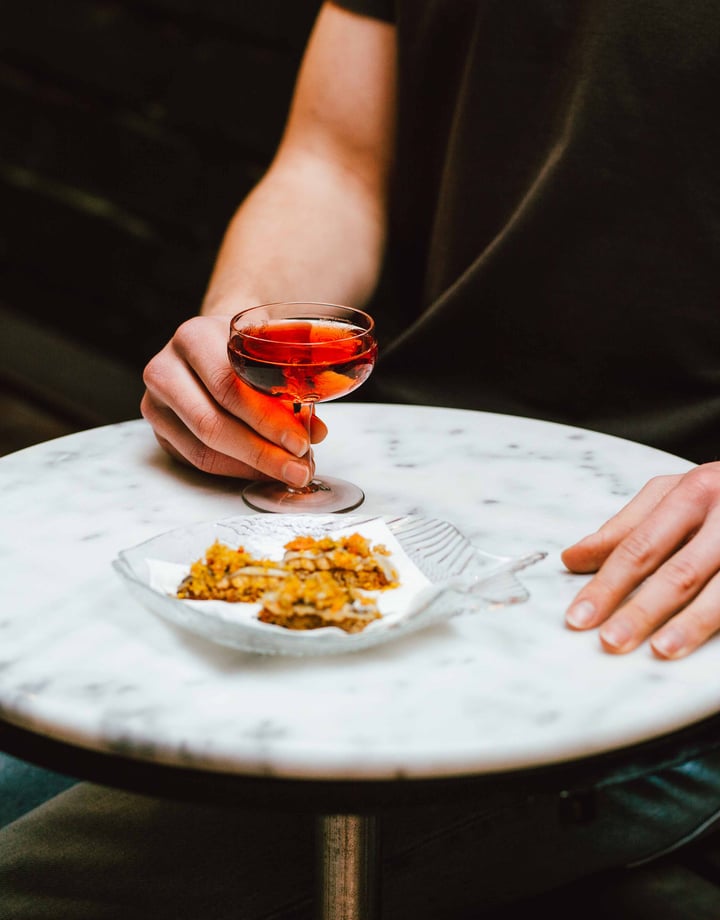 A hand holding a glass of rose next to a plate of food.