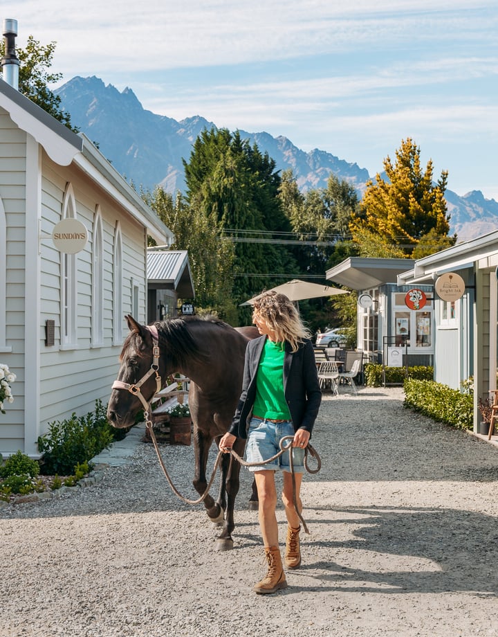 A woman and horse walking down a little country lane on a sunny day.