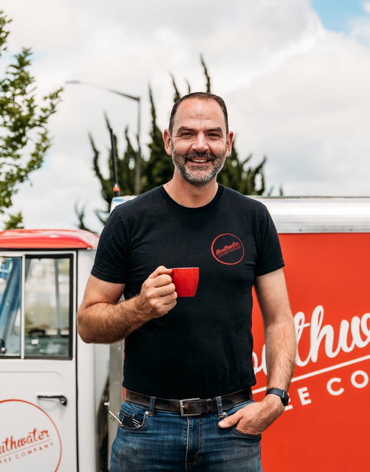 A man holding a red cup of coffee outside a coffee cart.