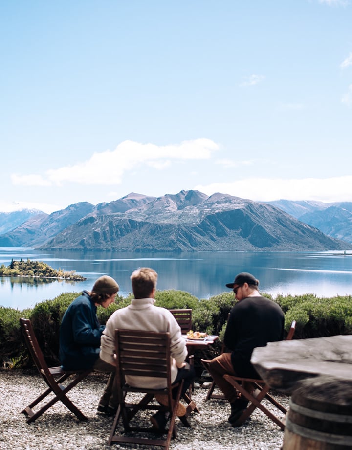 Jordan Siobhan Three men are sitting at an outdoor table overlooking the lake.