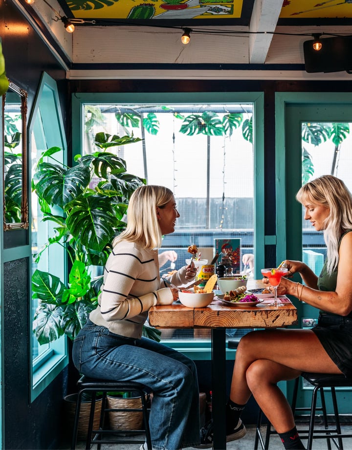Two women dining at a high table inside a green painted room.
