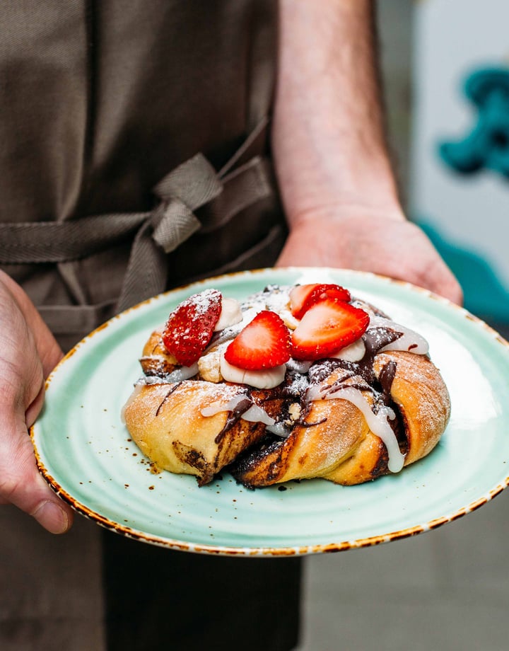 Two hands holding a vegan pastry on a plate.