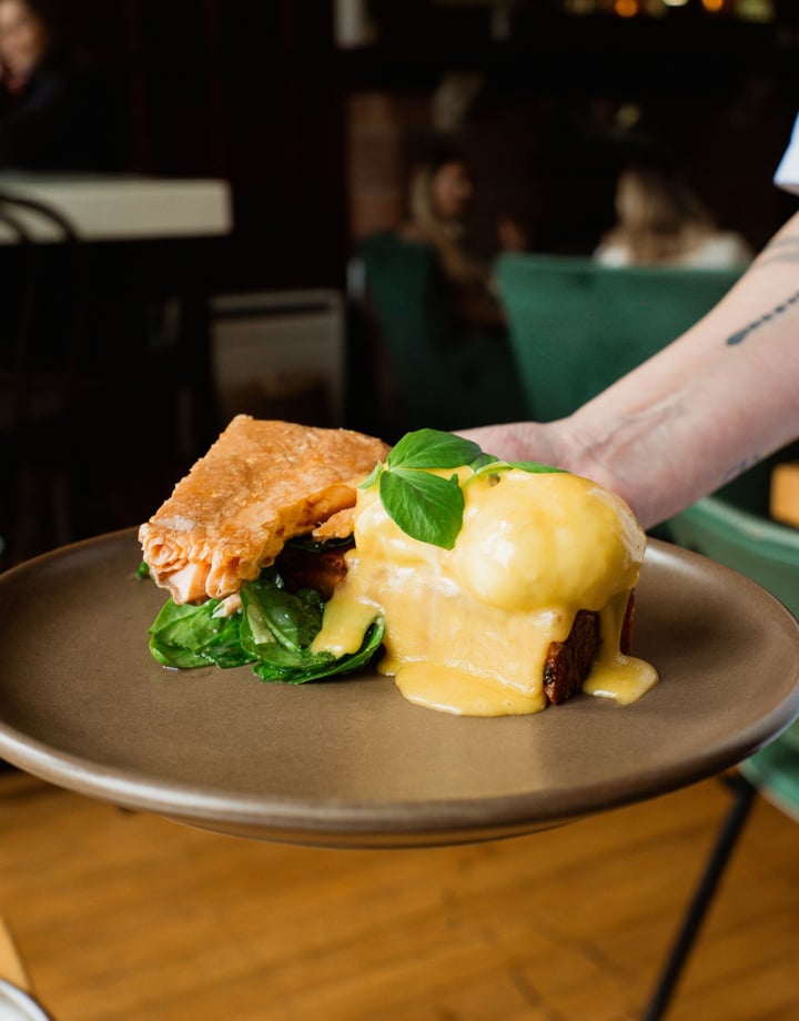Someone holding a plate of eggs hollandaise with smoked salmon on the side