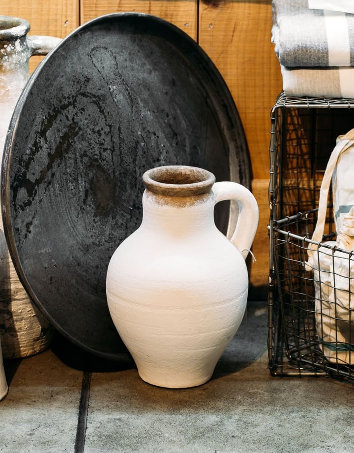 Two tall white concrete look vases on the floor next to a wire basket.