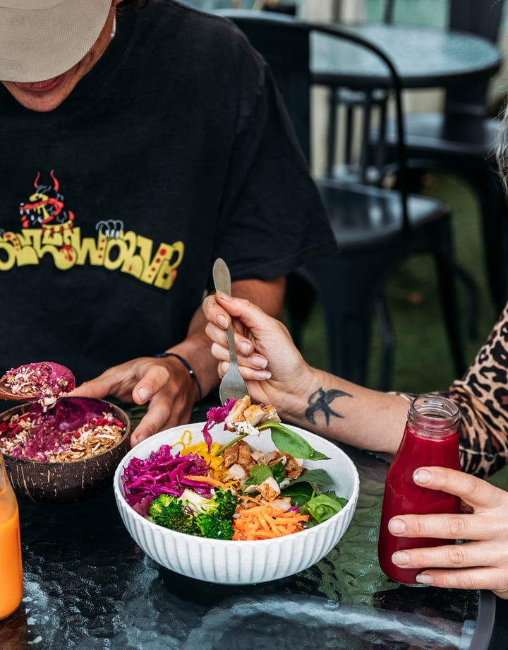 Two customers are eating buddha bowls and a glass bottle of juice is on the table.