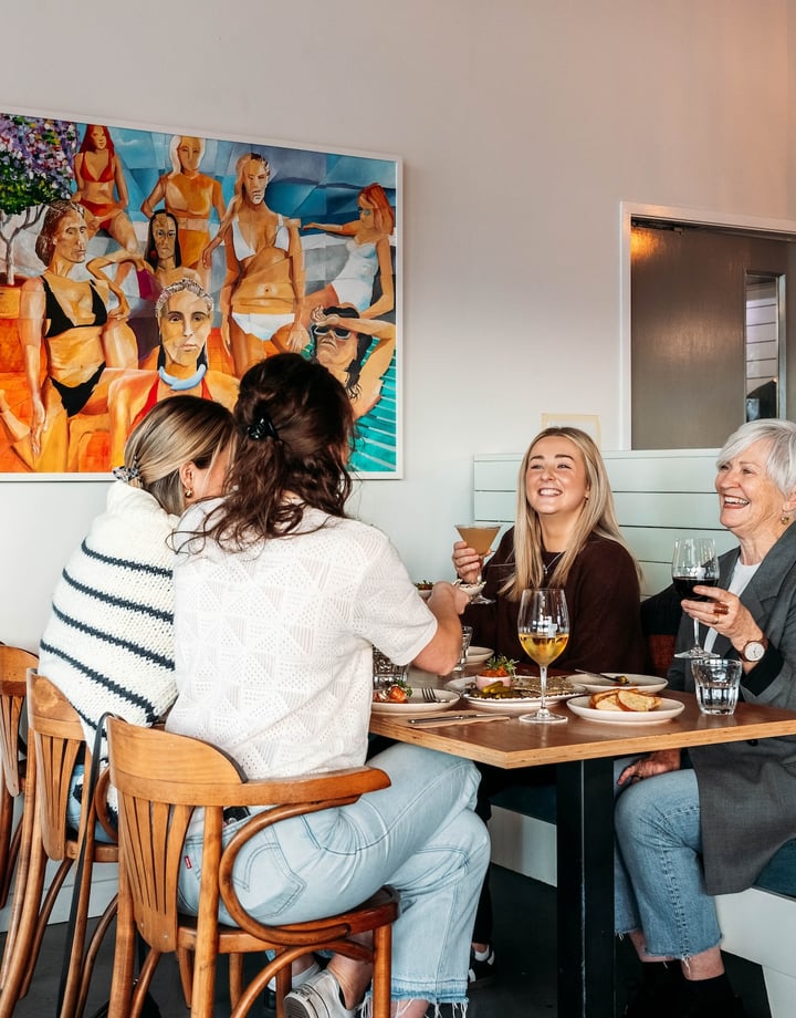 A group of women cheers their drinks over a table of food.