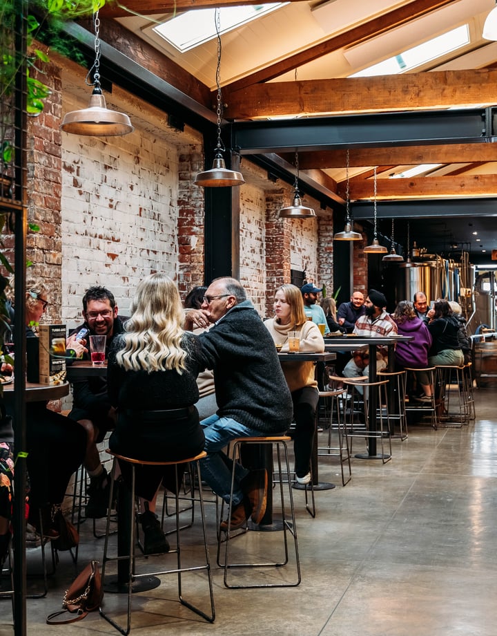 People sitting at high tops in a brick brewery building.