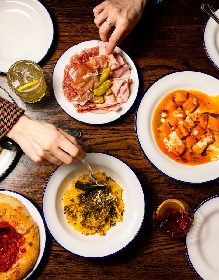Flat lay of table full of Italian dishes at Bar Franco with people digging in with their forks