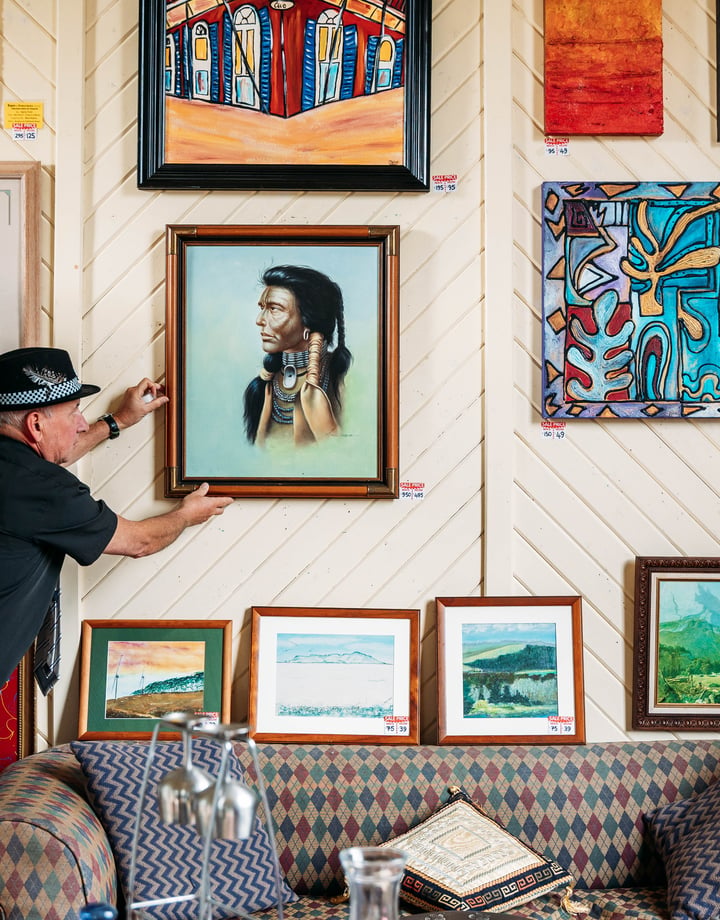 A man hanging art work on a wall inside a gallery.