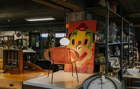 Vintage chair with retro painting of clown's face behind it at La Voute, Christchurch.