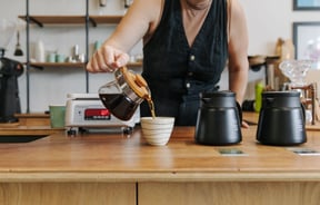 A woman pouring black coffee into a cup.