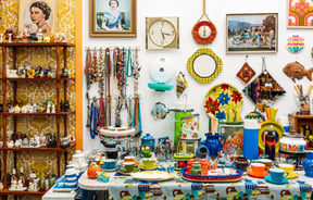 Eclectic mix of ceramics and vintage prints on walls and shelves of vintage secondhand shop