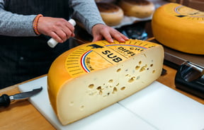 Someone slicing a wheel of Dutch cheese in specialty food store