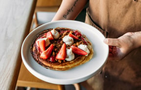 Someone holding a plate of pancakes with strawberries at cafe