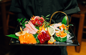 Square black plate with an arrangement of colourful foods reminiscent of what you would receive at Japanese restaurants.