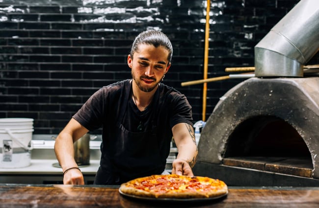 A chef serving a pizza fresh out of the pizza oven.