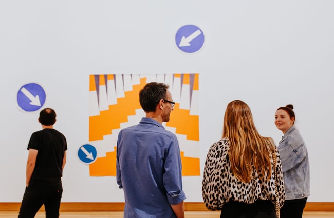 People viewing orange artwork inside the Christchurch Art Gallery.