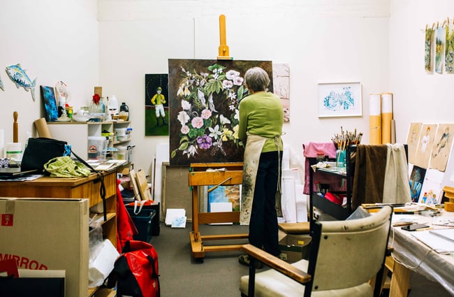 A woman painting on a canvas thats propped up on a wooden art easel.