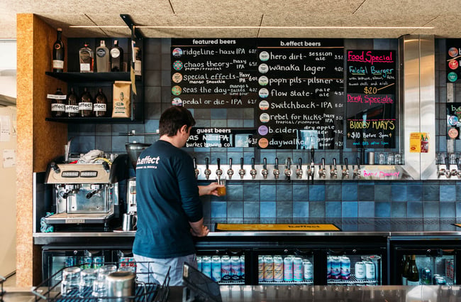 A male staff member pours a beer from a tap behind the counter at b.social, Wānaka.