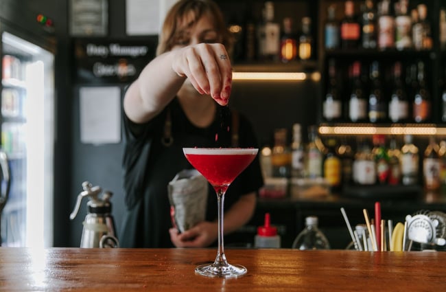 A bartender sprinkling some dried berries on top of a pink cocktail at the bar.