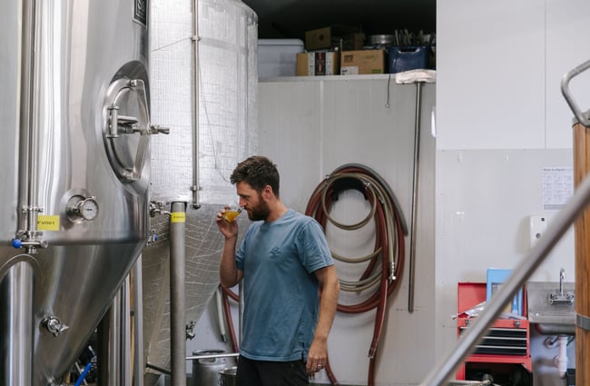 Man sniffing beer next to brewing vat.