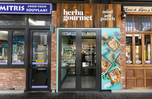 Exterior, footpath view of the Herba Gourmet store in Christchurch, with its bright wall signage.
