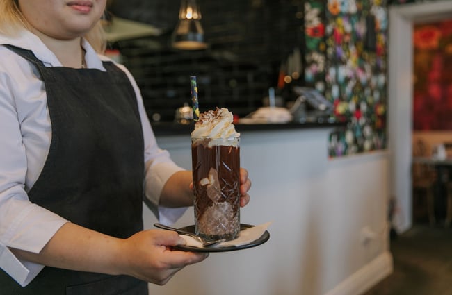 A waiter holds a large iced chocolate with whipped cream on top at Little Poms café, Christchurch.