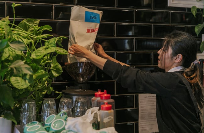 A barista pours Supreme coffee beans from a bag into the coffee grinder.
