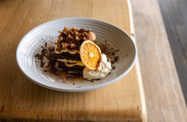 Close up of a plate of layered tiramisu waffles presented with whipped cream and a dehydrated orange slice.