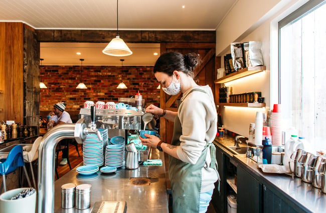 A staff member pouring milk into a coffee behind the counter at Punnet Eatery.