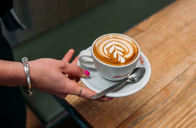 Close up of a hand holding a white coffee with barista art.