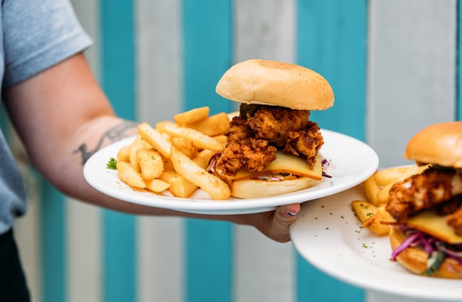 An outstretched arm holds two plates of fried chicken burgers and thick-cut chips at Seashore Cabaret in Petone.