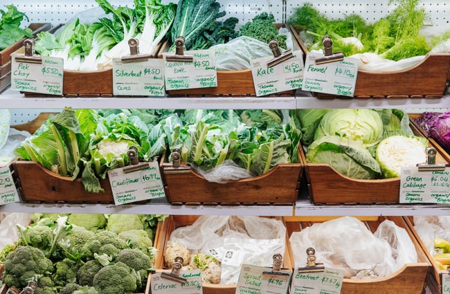 A full shelf of green vegetables in wooden boxes.