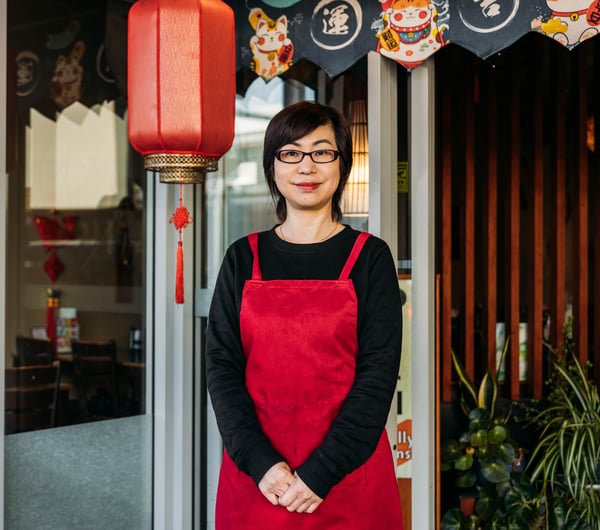 A woman dressed in red and black standing outside a Chinese restaurant smiling to camera.