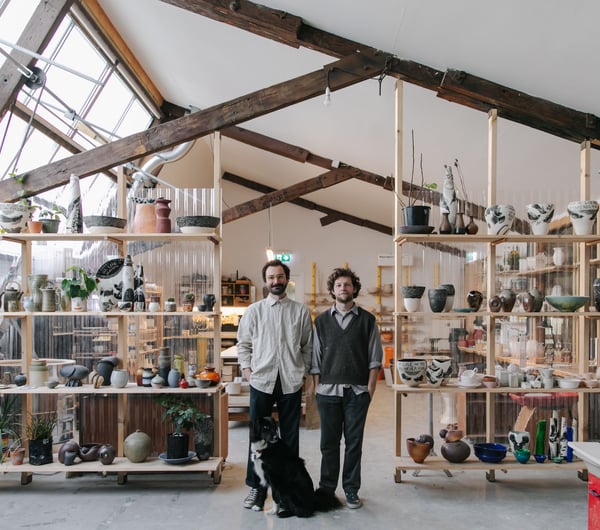 Jamie Smith and Tom Baker of Kiln Studio standing in their studio with a black dog.