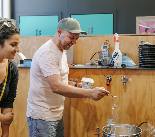 A person in a white t-shirt sprinkling baking soda into a brewing canister.
