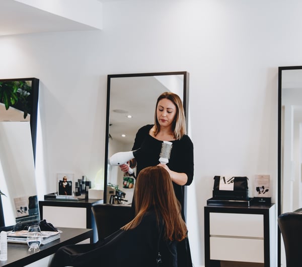 A woman blow drying hair inside Mod's Merivale hairdresser in Christchurch.