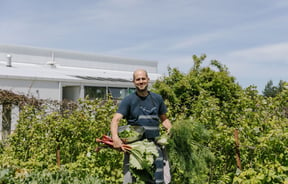 Bevan Smith from Riverstone Kitchen wearing a blue t-shirt and apron smiling to camera in amongst green trees.
