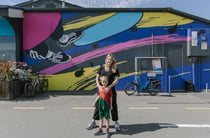 A woman and her son standing in front of a colourful mural painted on the exterior of a building.