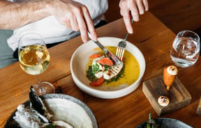 High angle view of a person cutting into a fish and citrus dish, wine and other dishes on the table at arc, Wānaka.