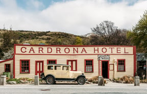 Historic cream and maroon weatherboard frontage of Cardrona Hotel with a vintage cream 1968 Chrysler Model 62 parked in front.