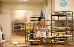A female chef moves a tray of proving dough rolls.